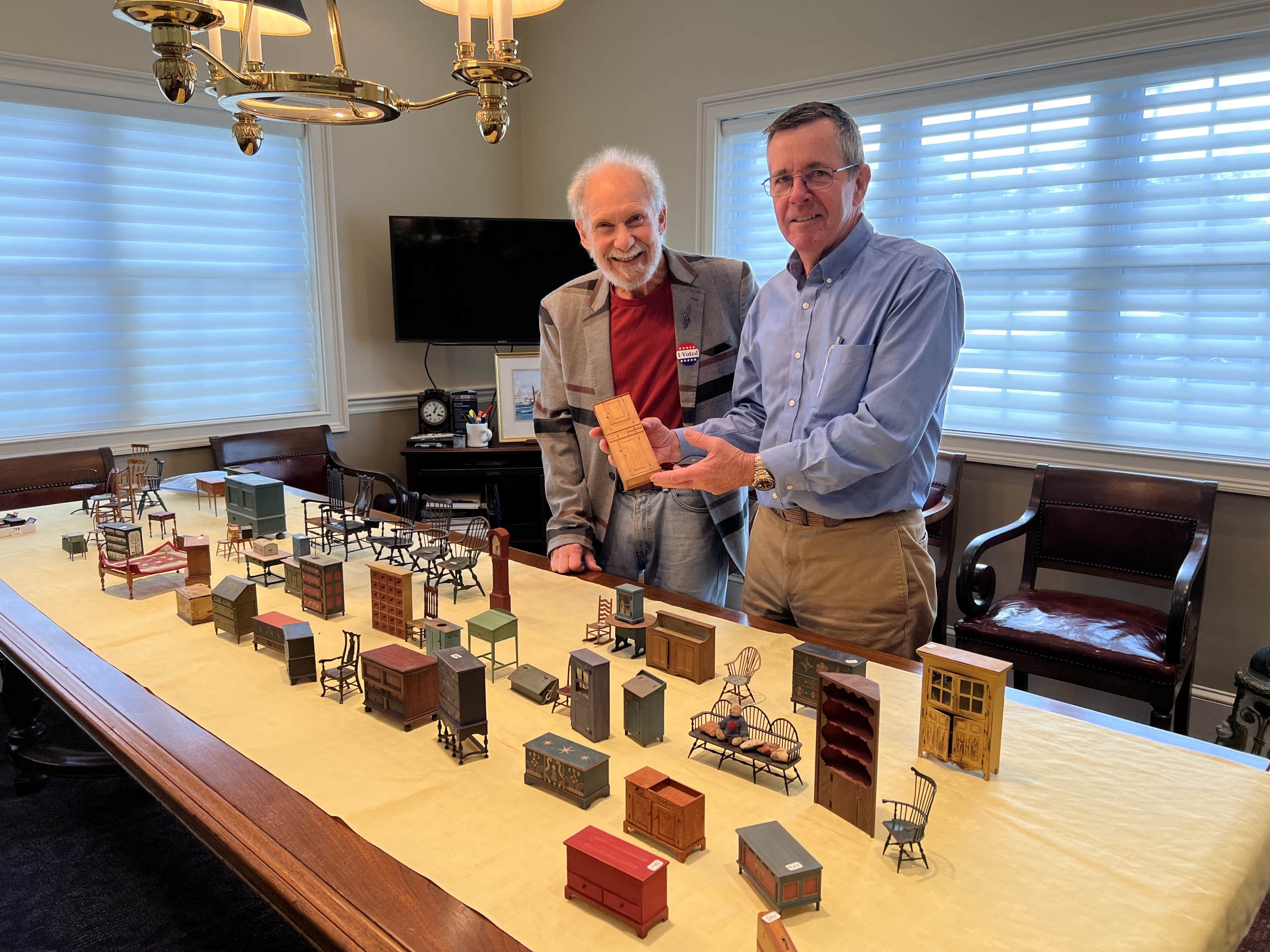Two people standing holding miniature furniture available for auction